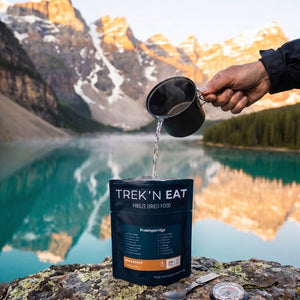 Trek'n Eat Proteinporridge gevriesdroogde ontbijt stazak wordt bereid met heet water bij een bergmeer