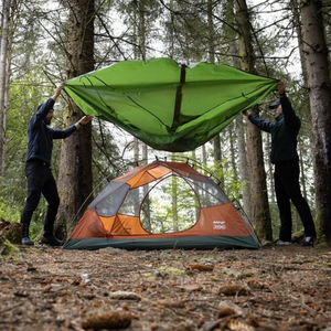 Twee personen die de buitentent van een Vango tent over de binnentent spannen in een bosrijke omgeving