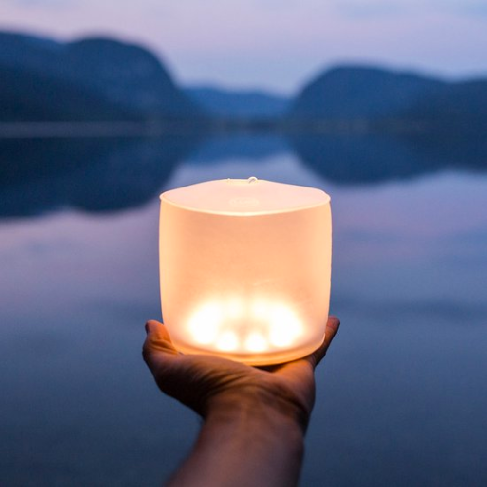 Hiker met rugzak loopt door bergachtig landschap en draagt een brandende MPOWERD Luci opblaasbare LED-solarlantaarn
