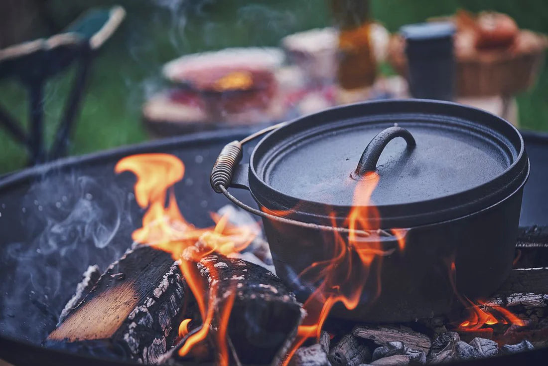 Een gietijzeren Dutch oven die boven een brandend kampvuur kookt in de buitenlucht